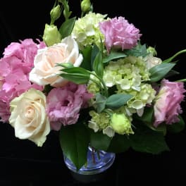 Low arrangement of cream roses, pink lisianthus, and green hydrangeas in a clear glass vase