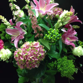 Tall arrangement of pink lilies and hydrangea with white blooms in a clear glass vase