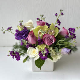 Mixed bouquet of roses, orchids, and purple blooms in a white vase
