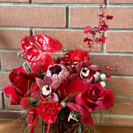 Red floral arrangement in a dark vase with roses and orchids