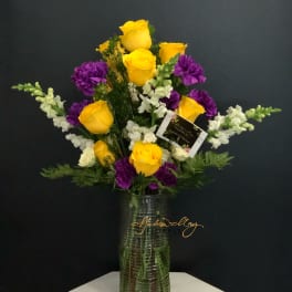 Yellow roses and purple carnations in a clear glass vase