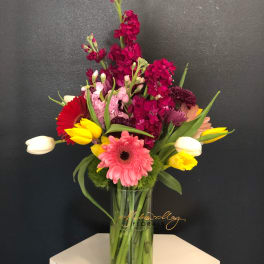 Mixed bouquet of pink, red, yellow, and white flowers in a glass vase