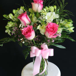 Pink roses and white alstroemeria in a glass vase with a pink ribbon