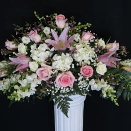 Pink roses and white flowers arranged in a white pedestal vase
