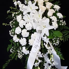 White funeral spray with lilies, roses, and carnations on a black background