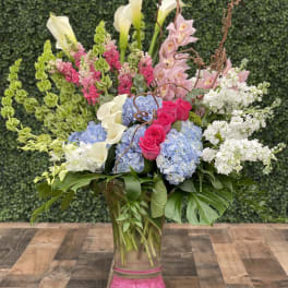 Tall mixed bouquet with pink roses, blue hydrangeas, white calla lilies, and orchids in a glass vase
