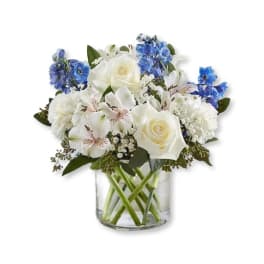 White roses and blue flowers arranged in a clear glass vase