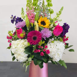 Mixed bouquet in a pink vase with sunflowers, roses, hydrangeas, and purple blooms