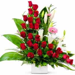 Tall arrangement of red roses, white lilies, and pink gerbera daisies in a white vase