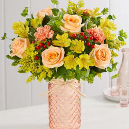 Peach roses and yellow flowers in a pink glass vase