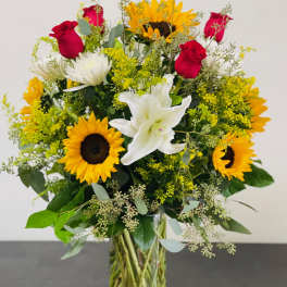 Bouquet of sunflowers, red roses, and white lilies in a glass vase