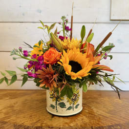 Mixed bouquet with sunflowers, roses, and purple blooms in a painted tin container