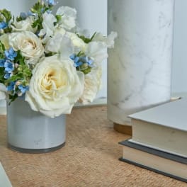 White roses and blue flowers arranged in a small vase on a table