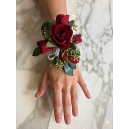 Red rose wrist corsage with white ribbon on a person's wrist