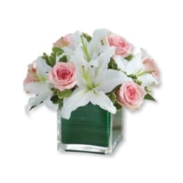 Pink roses and white lilies arranged in a clear square vase