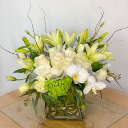 White and pale yellow floral arrangement in a square glass vase