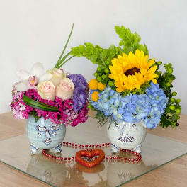 Two colorful floral arrangements in painted ceramic pots with a heart decoration