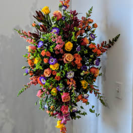 Tall multicolor standing spray with roses, lisianthus, and snapdragons on a black stand