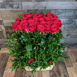 Tall arrangement of red roses atop dense green foliage in a rectangular basket