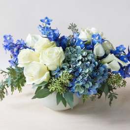 White roses and blue hydrangeas arranged in a low white bowl
