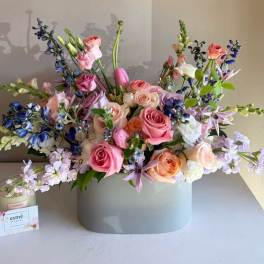 Pastel bouquet of roses, tulips, and blue flowers in a gray vase