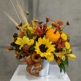 Fall floral arrangement with sunflowers, mums, and a small pumpkin in a metal bucket