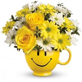 Yellow smiley-face mug filled with yellow roses and white daisies
