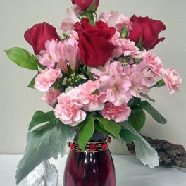 Red roses and pink flowers arranged in a burgundy vase