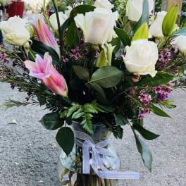 White roses and pink lilies arranged in a glass vase with a ribbon.