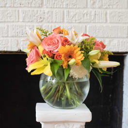 Mixed bouquet of pink, orange, and yellow flowers in a clear glass vase