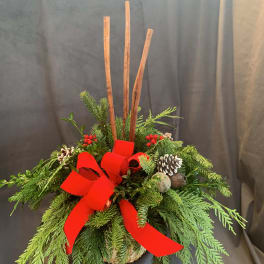 Evergreen arrangement with a red bow, pinecones, and tall sticks in a container