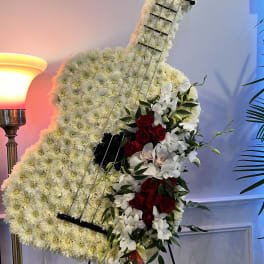 Guitar-shaped floral tribute with white flowers and red roses on an easel