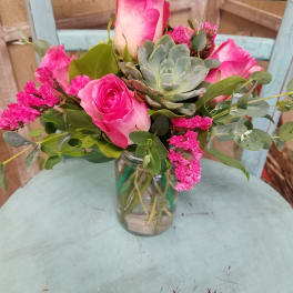 Pink roses and a succulent arranged in a glass jar vase