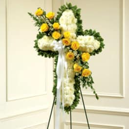 Cross-shaped floral tribute with white flowers and yellow roses on a stand