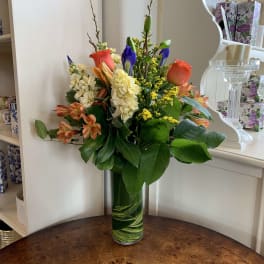 Mixed bouquet in a tall glass vase with orange, cream, and blue flowers