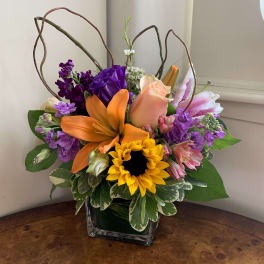 Colorful bouquet with orange lily, sunflower, and pink rose in a glass vase