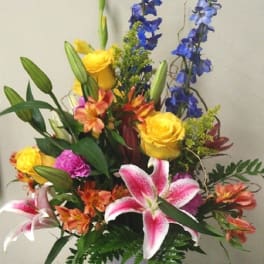 Mixed bouquet with yellow roses, pink lilies, and blue delphinium in a glass vase