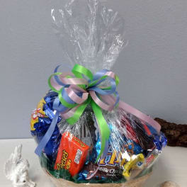 Basket of assorted candies wrapped in clear cellophane with a pastel ribbon bow
