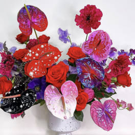 Bold arrangement of red roses and painted anthuriums with pearls in a white speckled vase