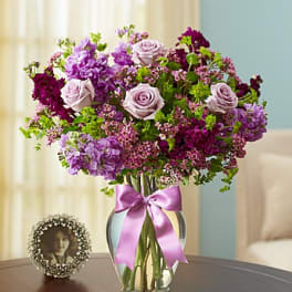 Lavender and purple bouquet in a clear vase with a pink ribbon