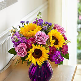 Bouquet of sunflowers and pink roses in a purple glass vase