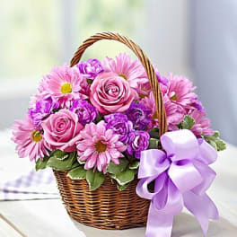 Pink and purple flowers in a wicker basket with a lavender ribbon