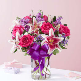 Pink roses and lilies in a glass vase with a purple ribbon