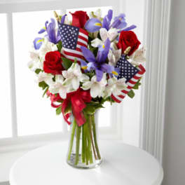 Bouquet of red roses and white lilies with small American flags in a glass vase