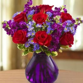 Red roses and purple flowers in a purple glass vase