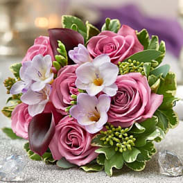 Pink roses with white orchids and dark calla lilies in a compact bouquet