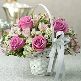 Pink roses and white alstroemeria in a white basket with a ribbon bow