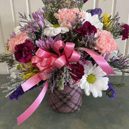 Mixed bouquet of pink, white, and purple flowers in a plaid container with a pink ribbon