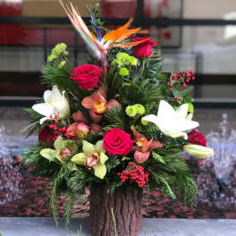 Tropical floral arrangement with roses, lilies, and orchids in a wood-look container