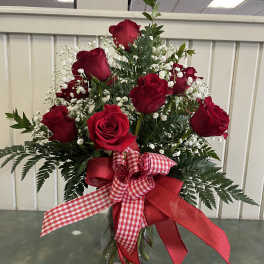 Red roses in a clear glass vase with white baby's breath and a red ribbon bow
